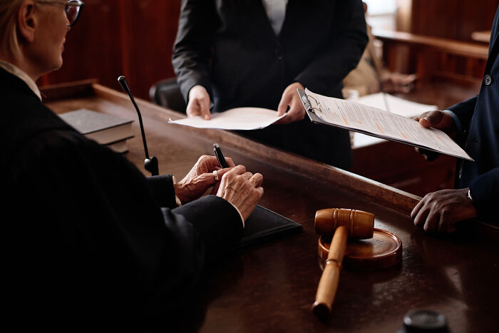 A judge in a courtroom, signing a document as lawyers present papers. Hardest cases require diligent legal work.