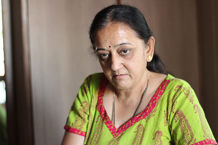 A woman wearing a green and pink patterned top, with dark hair, looking down with a serious expression, related to a Karen shames man eating meat.
