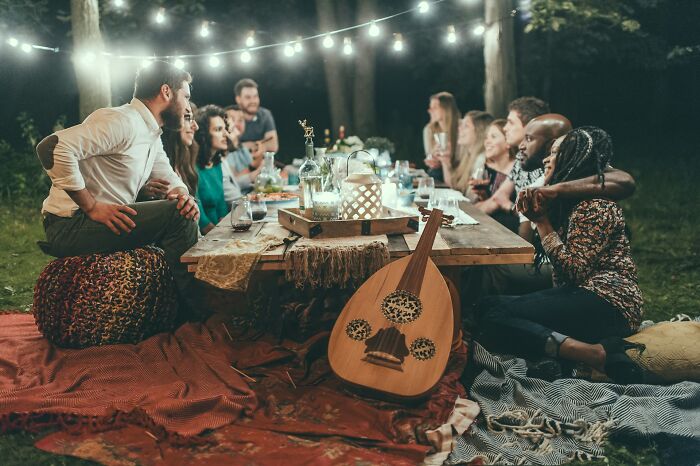 Friends enjoying an outdoor dinner under string lights, with an oud and wine. A silent luxury experience.