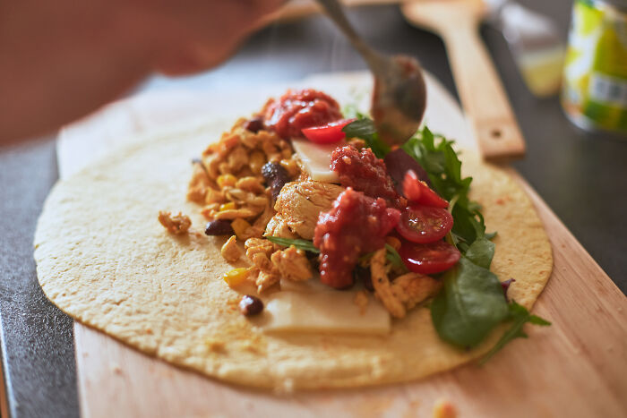 Cheap poverty meal chicken and salsa filling on tortilla wrap being spooned