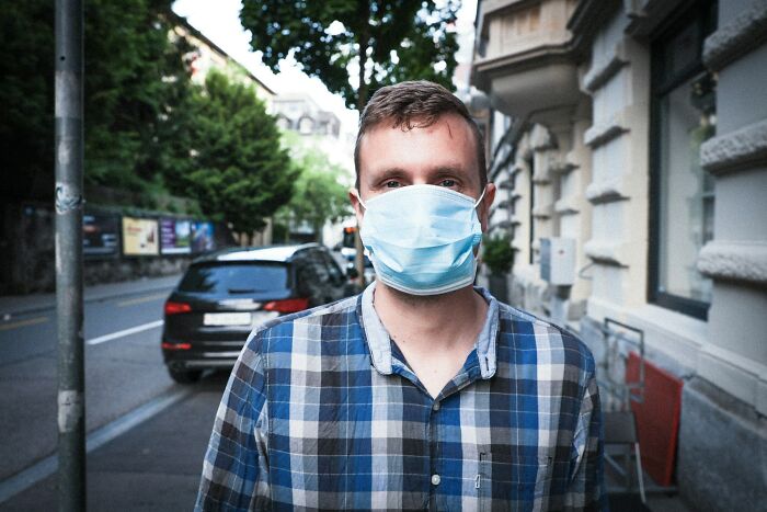 Man wearing a blue plaid shirt and a surgical face mask, looking directly at the camera. Represents men suffering and manosphere.