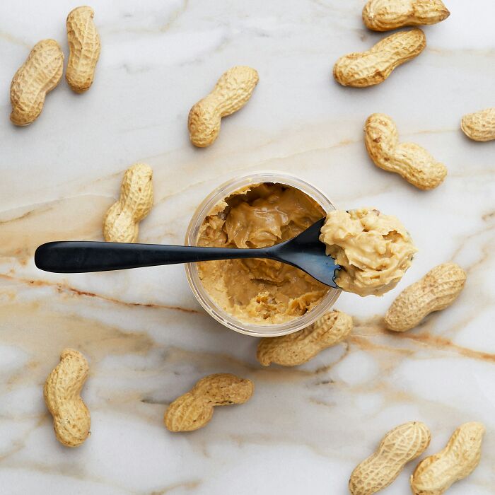 Peanut butter and whole peanuts on marble surface