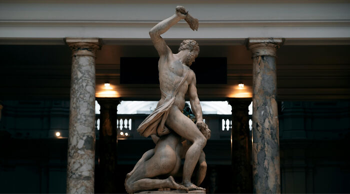 A classical marble statue of a muscular man raising an axe above a figure on the ground, representing an Oracle. A classical marble statue of a muscular man raising an axe above a figure on the ground, representing an Oracle.