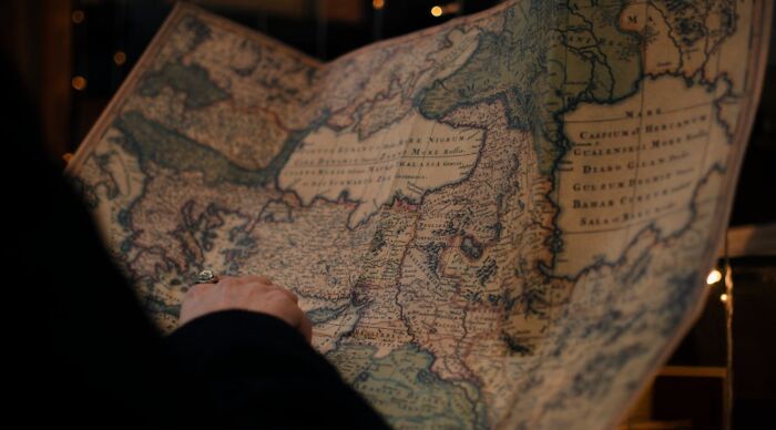 A person points to an ancient world map, engaging with a geography connections quiz. A person points to an ancient world map, engaging with a geography connections quiz.