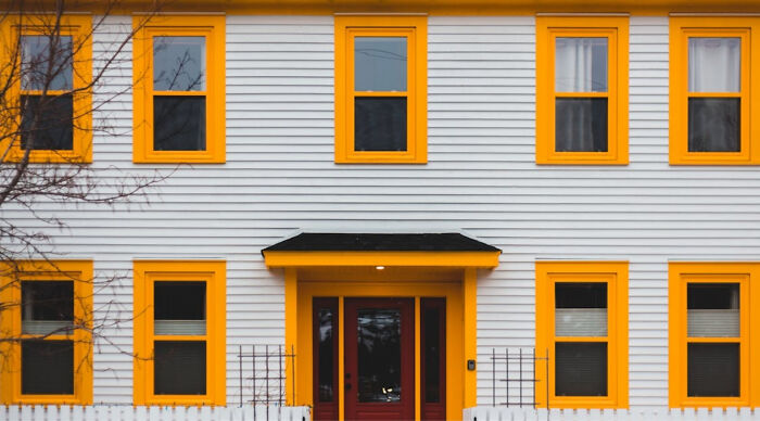 White house with bright yellow window frames and a dark red front door in clear daylight White house with bright yellow window frames and a dark red front door in clear daylight