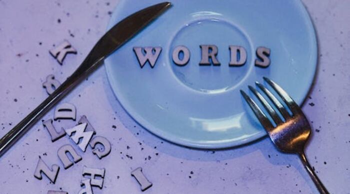 A blue plate with the word WORDS spelled out in wooden letters, surrounded by a fork, knife, and scattered letters, symbolizing vocabulary skills and compound word puzzles. A blue plate with the word WORDS spelled out in wooden letters, surrounded by a fork, knife, and scattered letters, symbolizing vocabulary skills and compound word puzzles.
