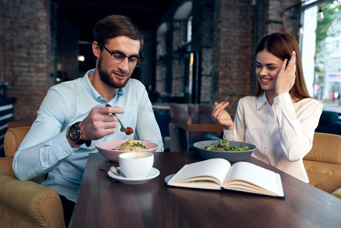 A man and woman sharing a lunch invite in a cafe, suggesting a potential date or misunderstanding.