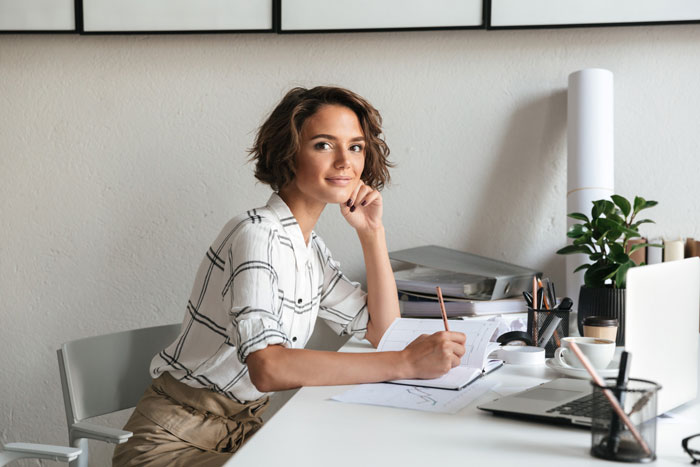 A woman in a white plaid shirt writing in a notebook at a desk. She realizes a casual lunch is a date.