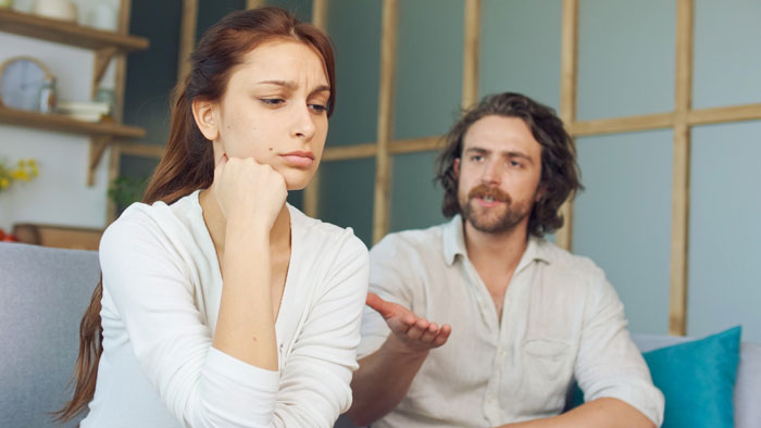 A woman looking distressed with her hand on her chin, a man gesturing in the background. Is it a date?