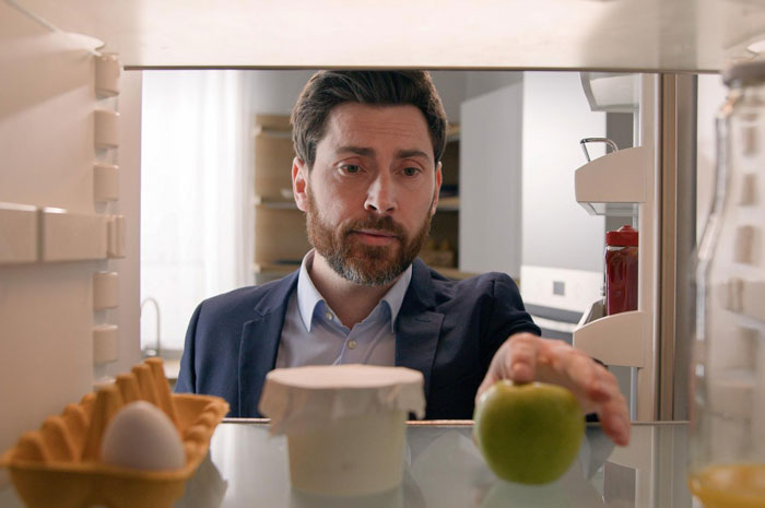 A man with a beard looking into a refrigerator, reaching for a green apple, an Office Food Thief in action. A man with a beard looking into a refrigerator, reaching for a green apple, an Office Food Thief in action.