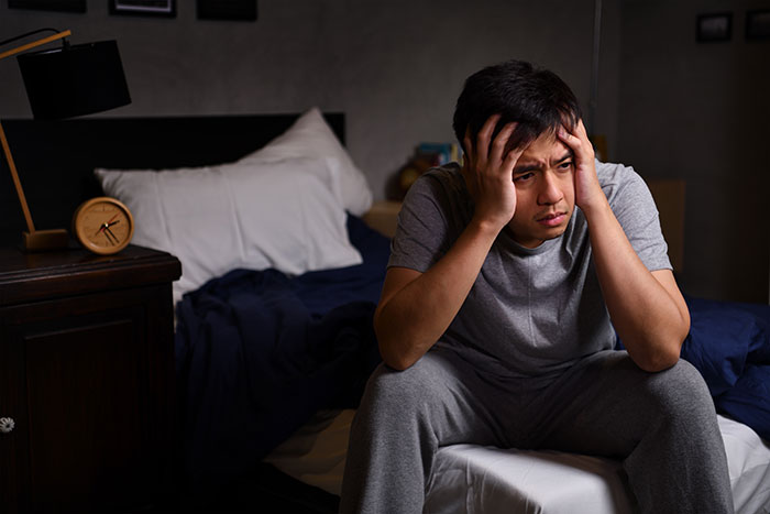 Stressed man sitting on bed with hands on head feeling distressed creepy things women have done
