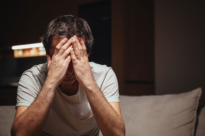 Man covering face in distress indoors, depicting emotional impact of creepy actions by women