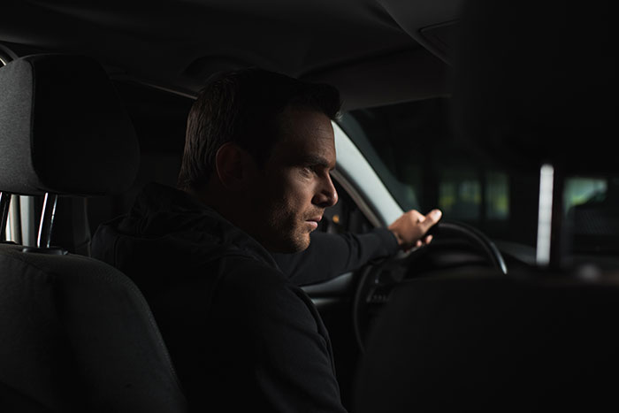 Man sitting alone in car at night feeling uneasy and creeped out