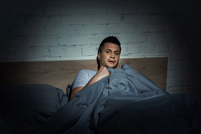 Anxious man in bed clutching blanket at night haunted by creepy women actions
