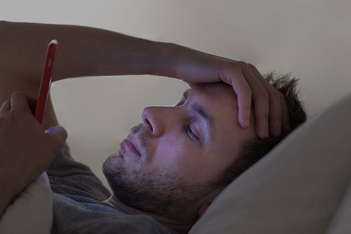 Man looking at phone in bed feeling creeped out by women actions