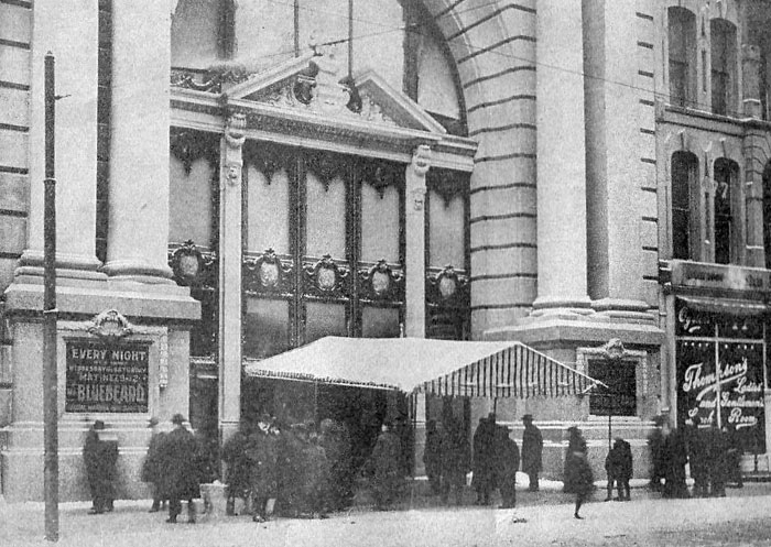 Black and white historic photo of people standing outside a large building entrance