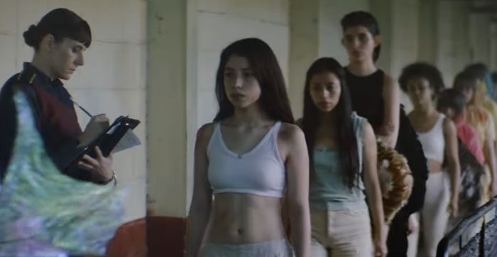 Young women standing in line under watchful officer in dark rabbit holes