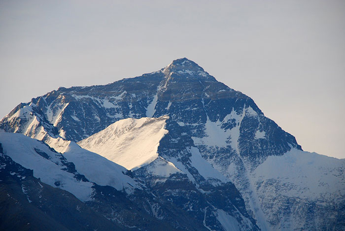 Snow-covered Mount Everest peak towering under cloudy sky