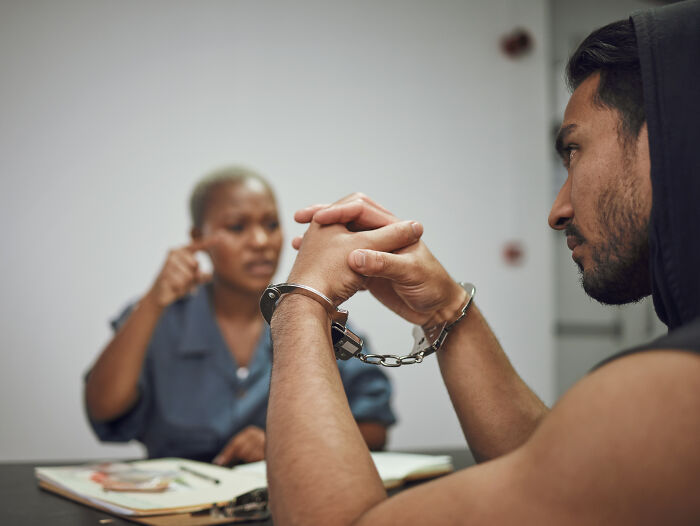 A man in handcuffs being interviewed by a lawyer, illustrating the hardest cases lawyers had to defend.