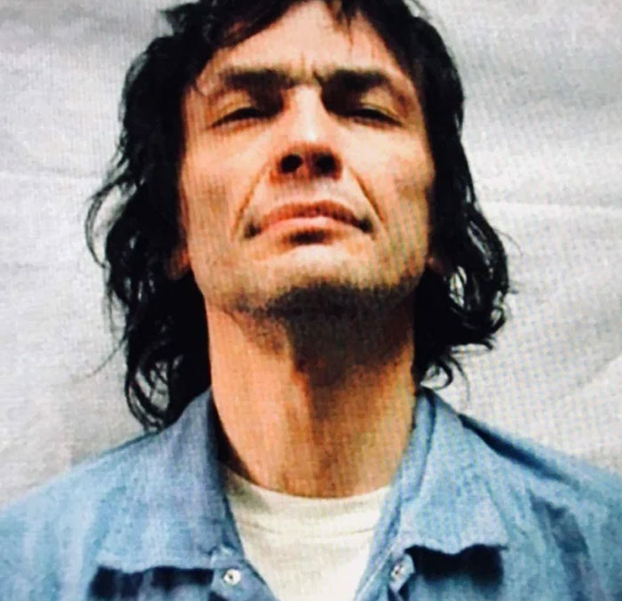 Mugshot of man with long hair and blue shirt for serial killers facts