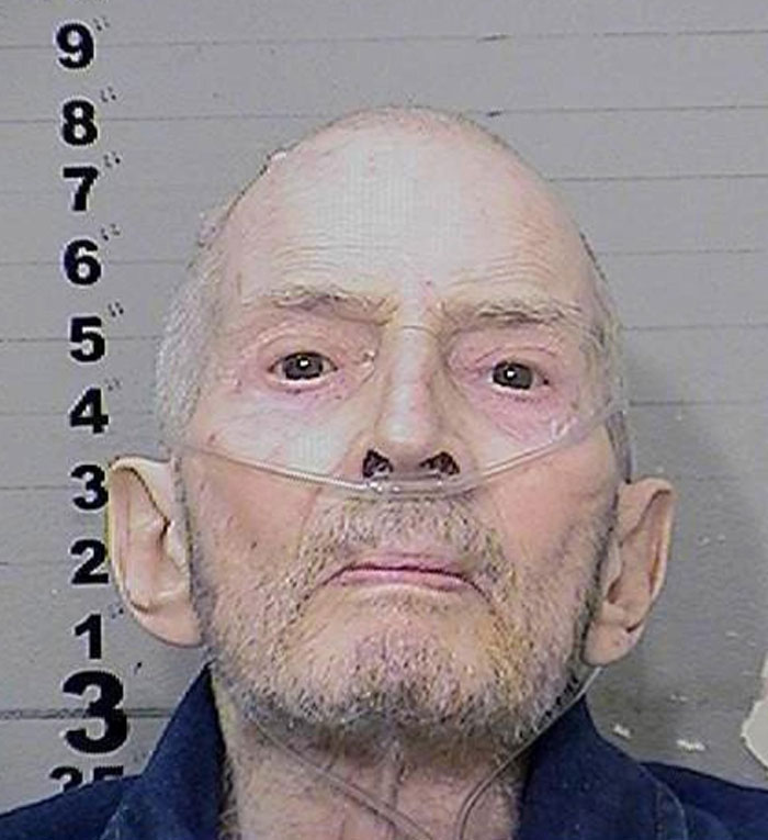 Elderly serial killer in oxygen mask against height chart background