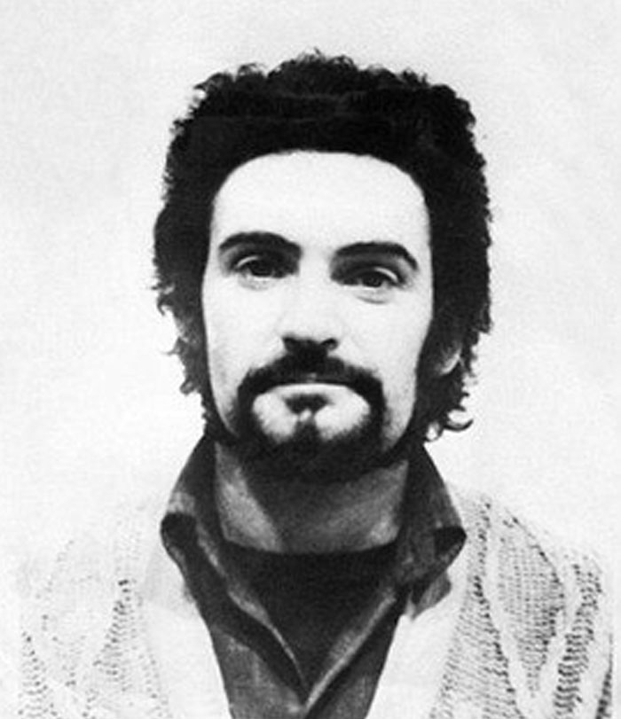 Black and white mugshot of a serial killer with beard and curly hair