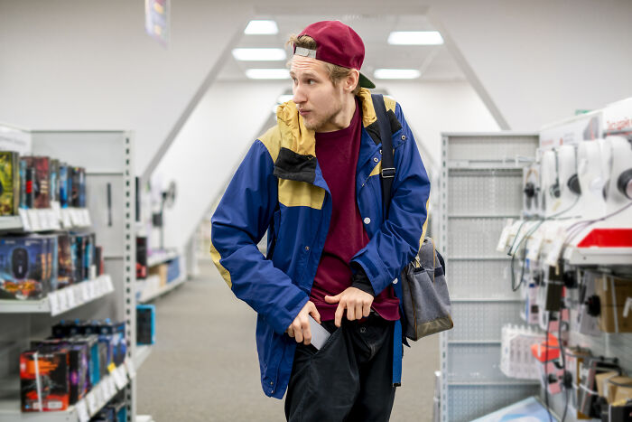 A young man, wearing a blue and yellow jacket, stealing from a store, looking around cautiously. Hardest cases to defend.