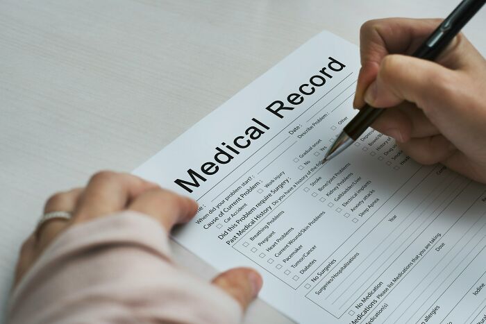 Hands filling out a medical record form with pen