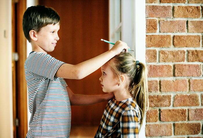Boy measuring girl's height with pencil indoors