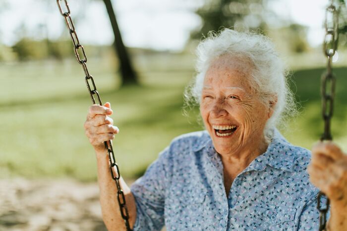 Smiling elderly woman enjoying swinging in an outdoor park