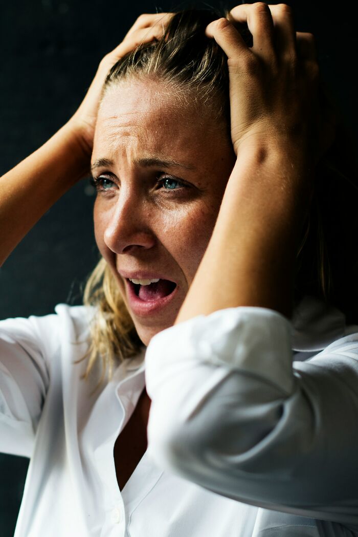 Distraught woman with hands clutching her hair, crying out, representing truly disturbing d***h stories.