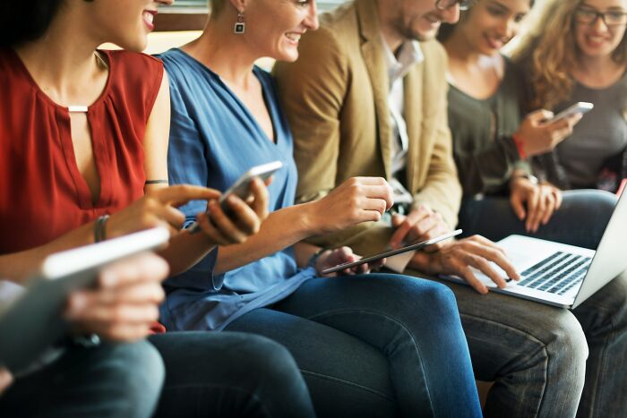 Group of young adults using various digital devices on a couch, illustrating social technology use
