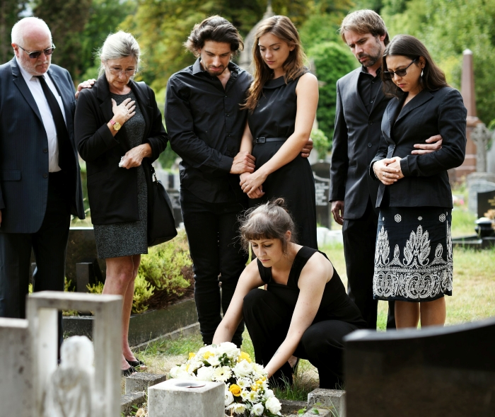 Group of mourners at a gravesite laying flowers during funeral
