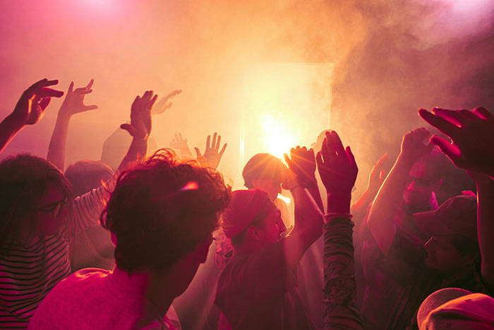 A crowd of people dancing with their hands raised in the air, bathed in orange light and smoke. Arts lovers may be younger. A crowd of people dancing with their hands raised in the air, bathed in orange light and smoke. Arts lovers may be younger.