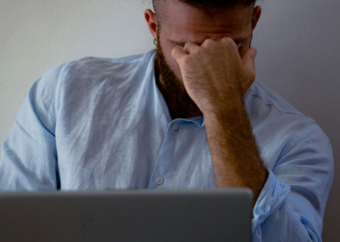 Stressed man covering face sitting at laptop showing dark secrets stress