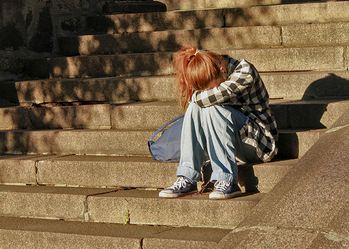 Sad person sitting on stairs hiding face reflecting dark secrets