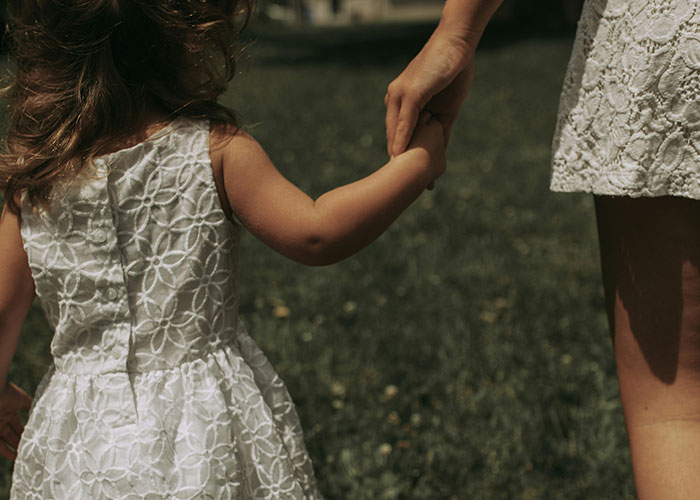 Adult holding hands with a young child in white lace dresses outdoors