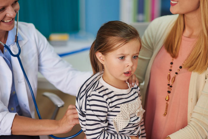 A child looking worried as a doctor uses a stethoscope, with an adult's hand on their shoulder. Discussing allergies.