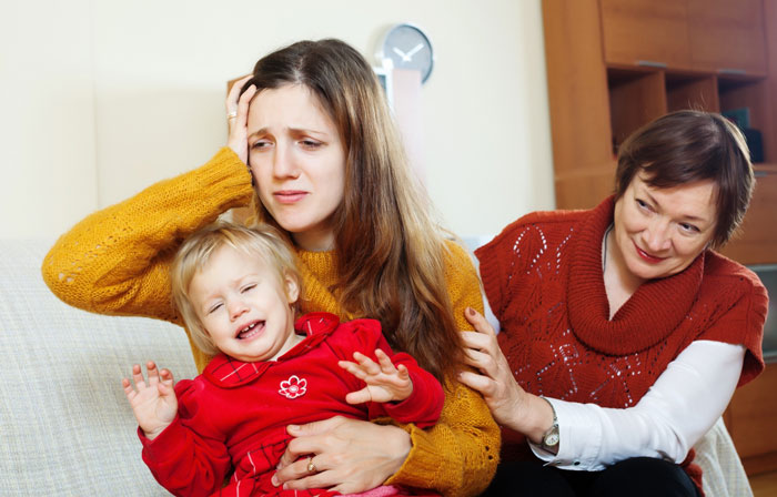 A stressed mother holds a crying child while a smiling grandma, who doubts the kids allergies, sits nearby.