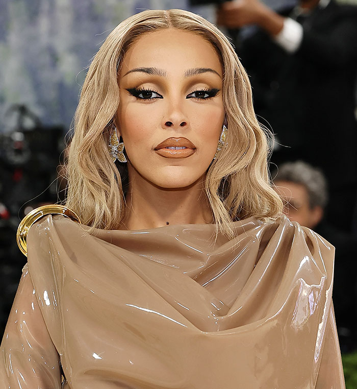 Doja Cat at Met Gala 2026, blonde hair, glossy lips, wearing a shiny beige gown. Focus on Plastic Surgery.