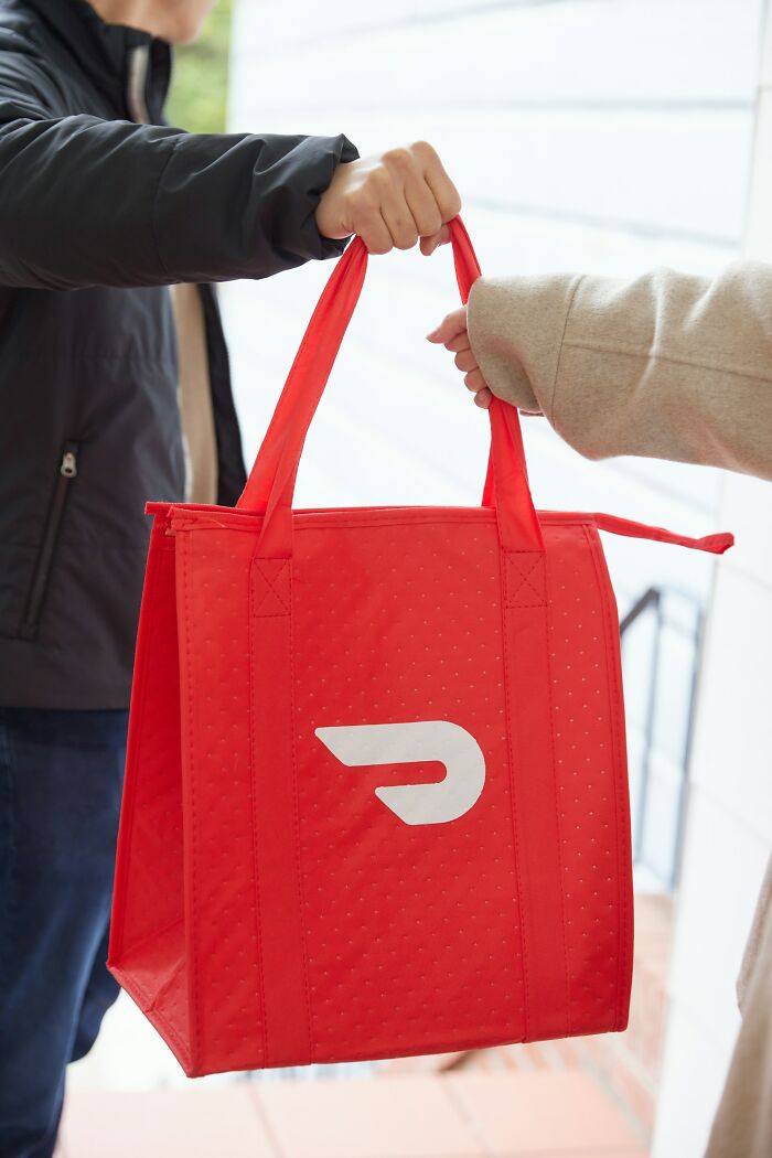Uma pessoa entregando uma sacola DoorDash vermelha para outra pessoa. Semelhante a histórias de flagrantes de traição de BF.