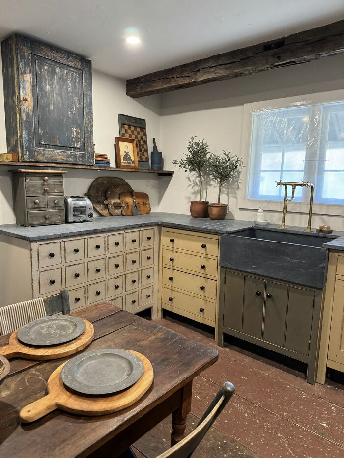 Historic American kitchen with various collected early America pieces, including a distressed cabinet, multi-drawer unit, and pewter plates.