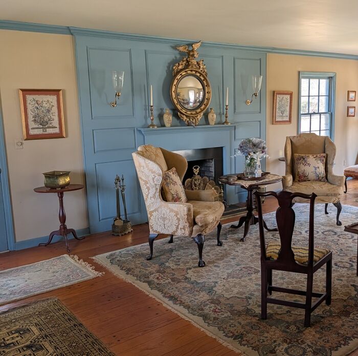 A historically decorated room featuring Early America pieces, including two armchairs and a fireplace with a gilded mirror.