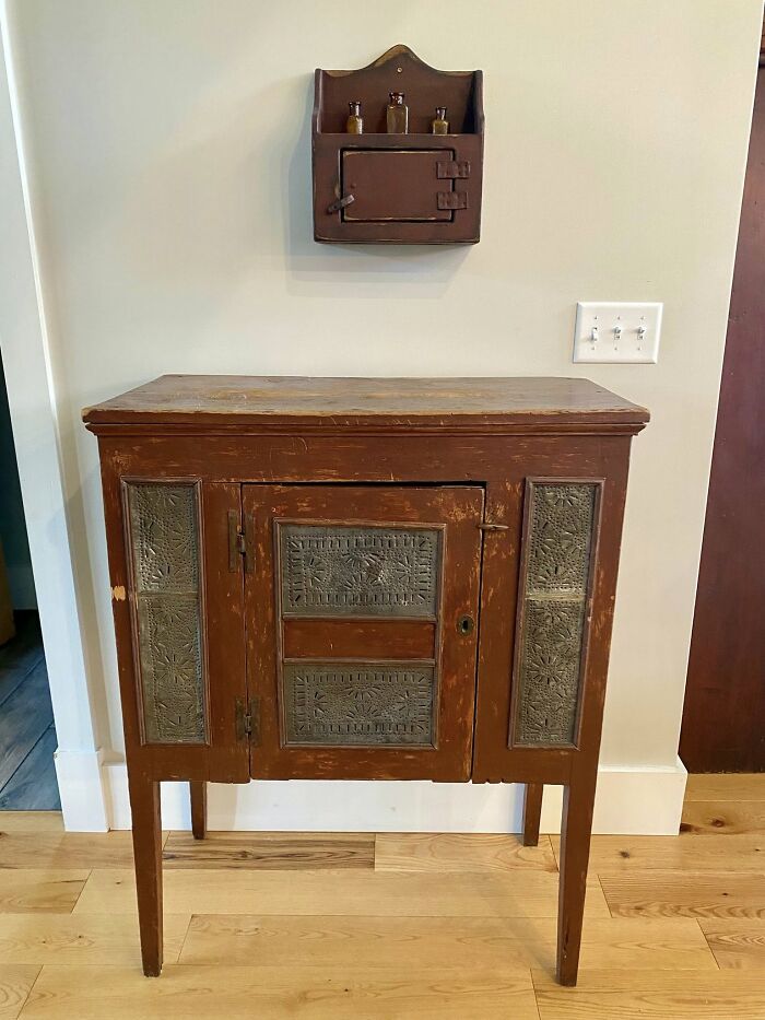 Early American furniture: a rustic red cabinet with punched tin panels and a matching wall shelf, showcasing historic pieces.