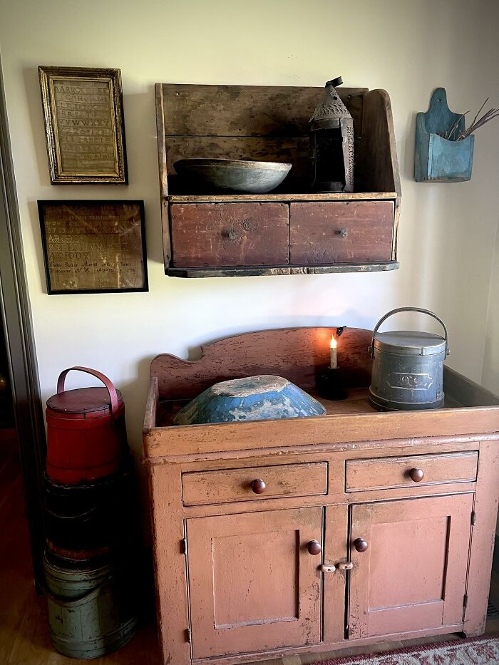 A collection of early America historic pieces, including antique furniture, bowls, and buckets, displayed in a rustic setting.