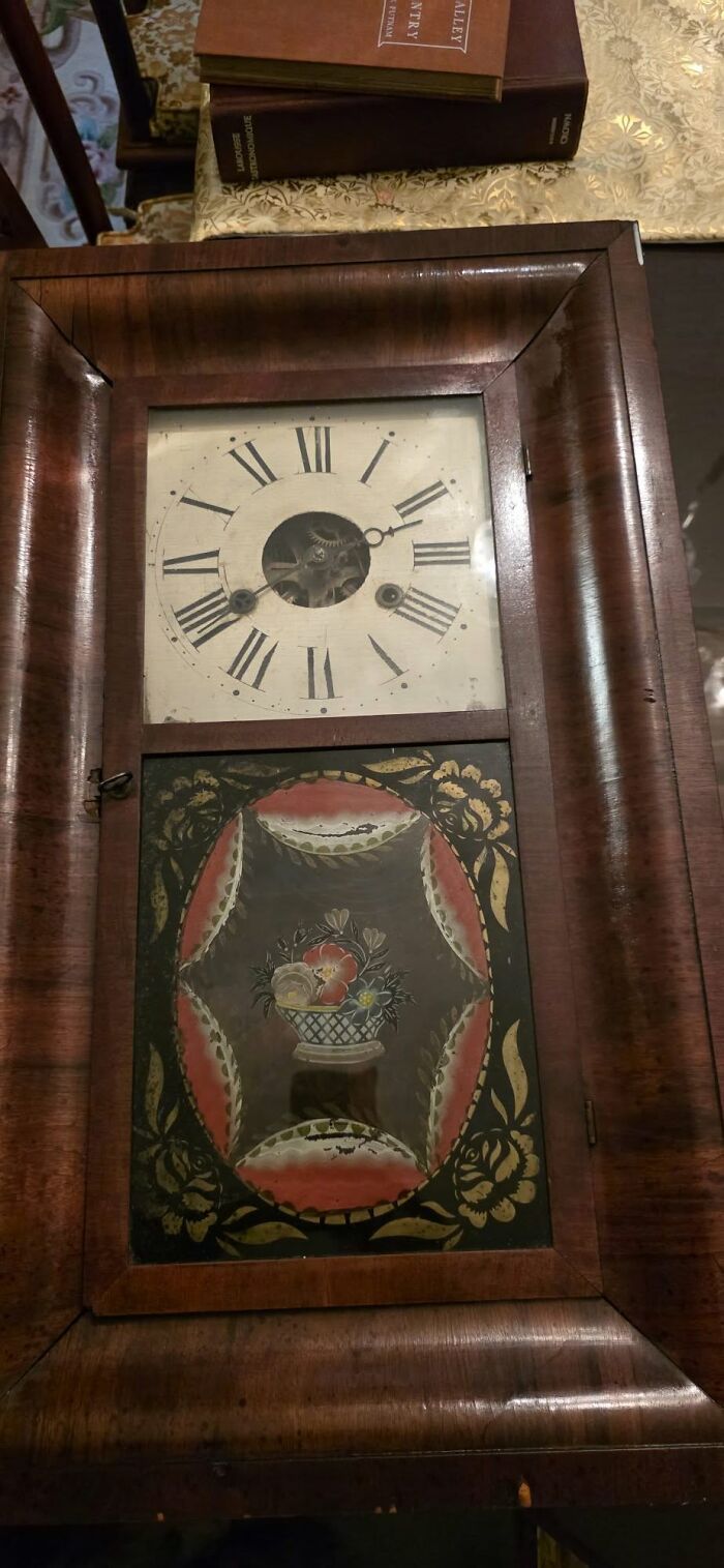 A close-up of an ornate historic American clock with a decorative painted glass panel. Early America collected item.