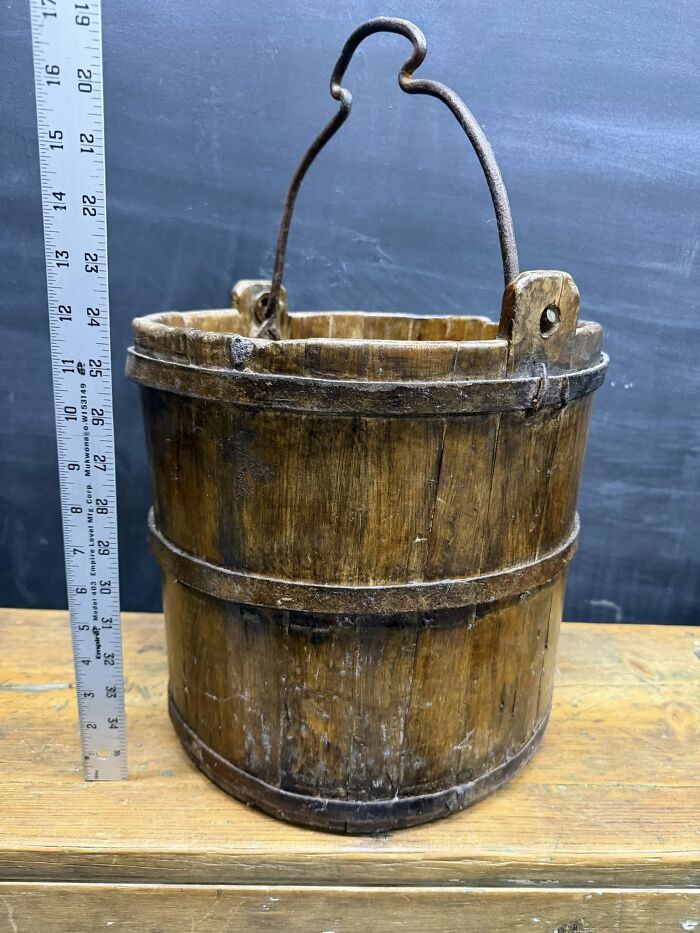 An antique wooden bucket with a metal handle, a historic piece from early America, on a wooden table.