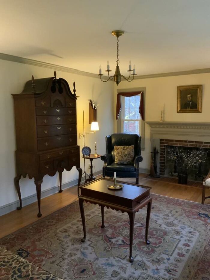 A room furnished with Historic Pieces From Early America, including a tall chest of drawers, a leather chair, and a fireplace.