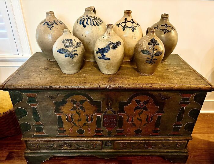 Several historic pieces from early America, including stoneware jugs with blue designs and a painted wooden chest.