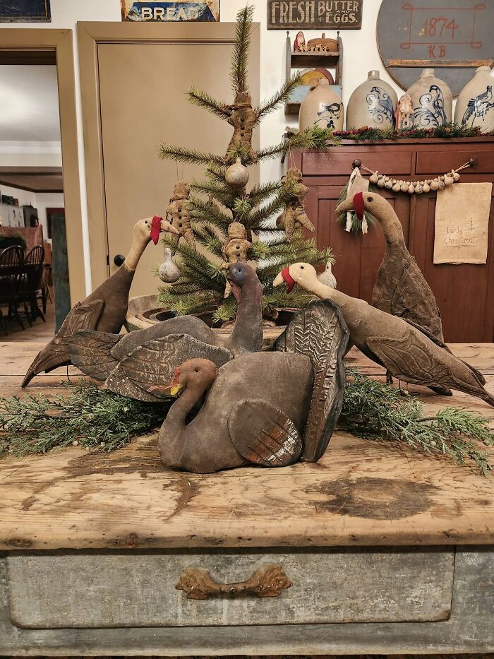 Antique turkey decoys surround a decorated tree, displaying historic pieces from early America in a rustic setting.